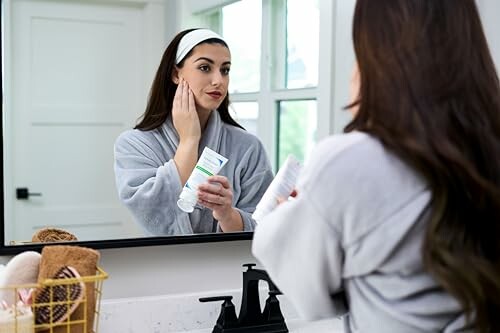 Woman applying skincare product in front of a mirror.